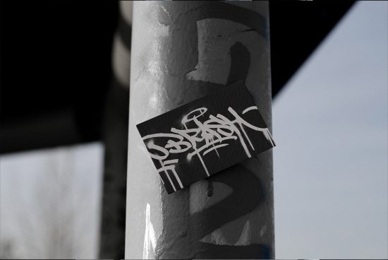 Urban graffiti sticker on a lamppost showcasing a black and white calligraphy design, ideal for mockup and graphic inspiration.