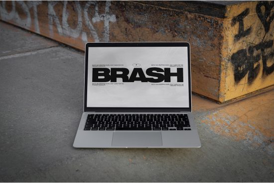 Laptop on urban ground displaying bold font design for 'BRASH', ideal for graphic design mockups, showcasing font styles in environmental context.