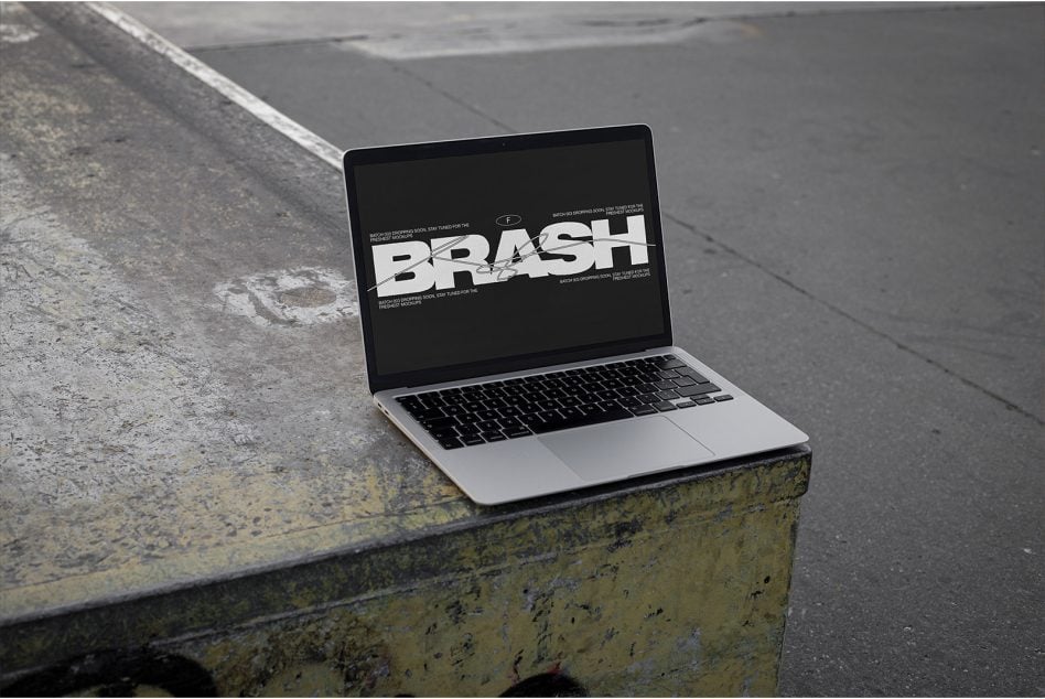 MacBook on weathered concrete ledge displaying BRASH design mockup on dark screen