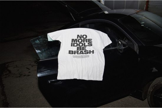 White t-shirt with bold slogan hanging on car door, urban night setting, apparel mockup, edgy streetwear design, graphic tee template.