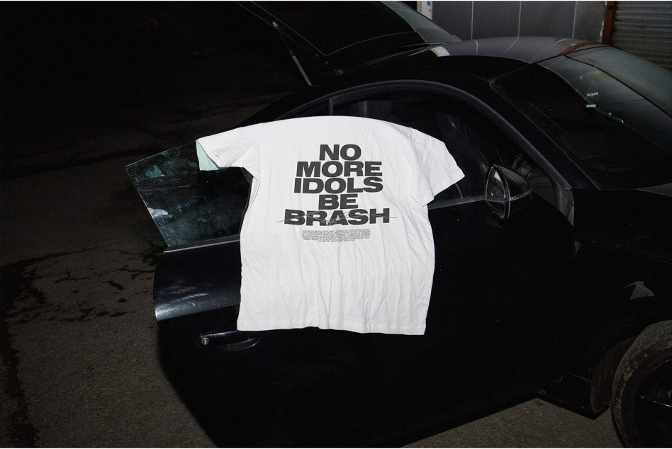 White t-shirt with bold slogan hanging on car door, urban night setting, apparel mockup, edgy streetwear design, graphic tee template.