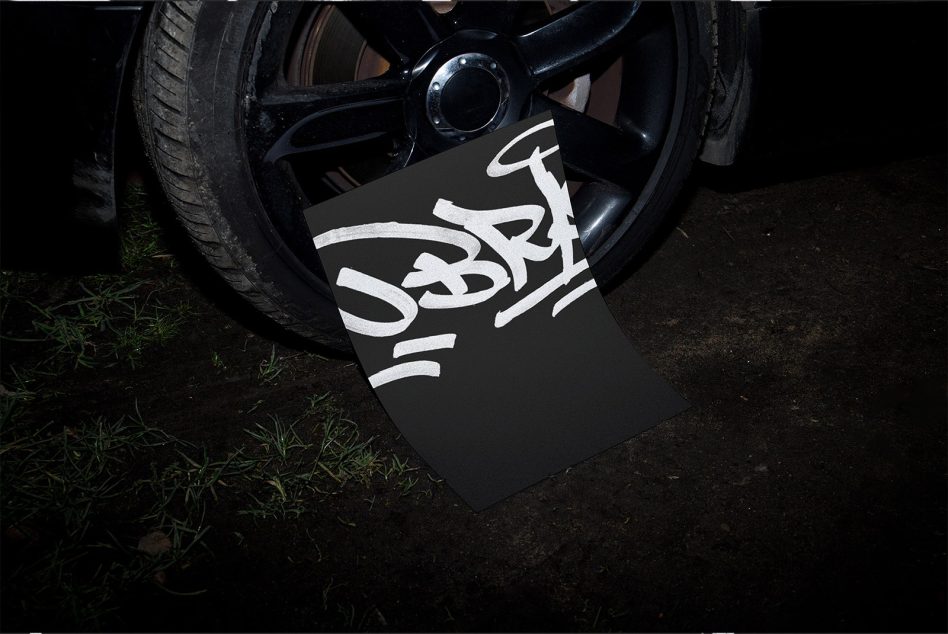 Dark paper mockup on car wheel showing white cursive script lettering design