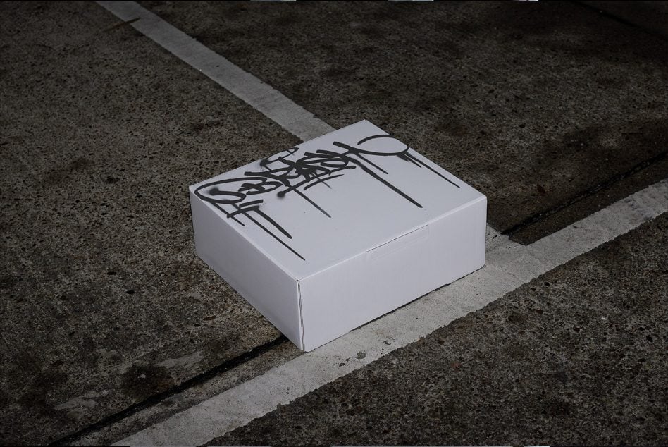 White shipping box with graffiti tag on asphalt parking lot