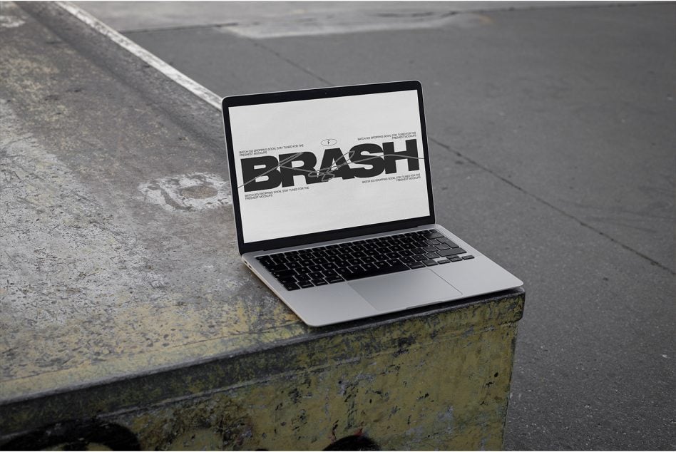 MacBook on weathered concrete ledge showing BRASH typography mockup on white screen