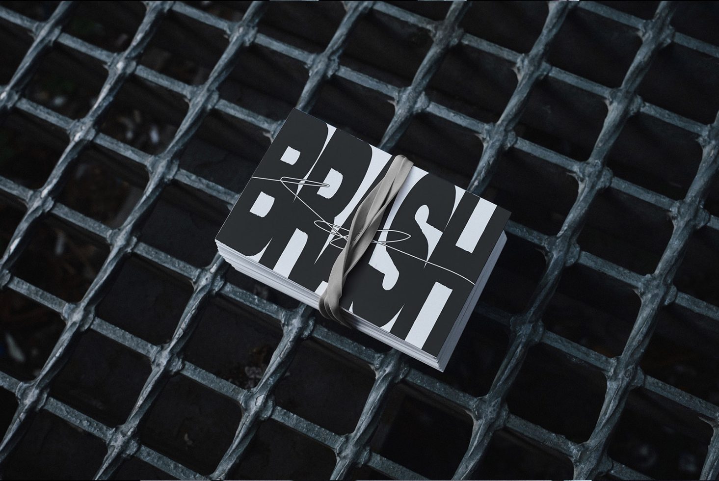 Stack of business cards with bold BRUSH font tied with ribbon on a metal grate; card mockup for designers; ideal for showcasing typography and graphic designs