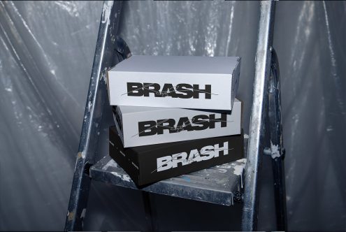 Stack of three shoe boxes with bold typographic design on a metal stair, industrial setting, ideal for packaging mockup.