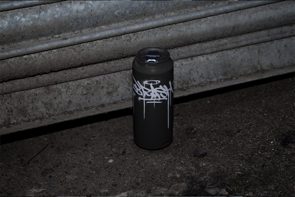 Black spray paint can with white graffiti tag on rough concrete surface