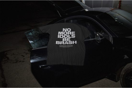 T-shirt mockup on car in urban night setting, bold text graphic design, edgy fashion presentation, dark moody atmosphere.