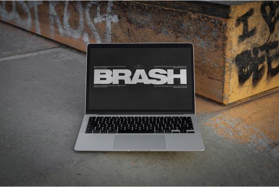 Laptop on urban ground displaying bold BRASH font design, ideal for Graphics category, eye-catching urban style font, editable text design.