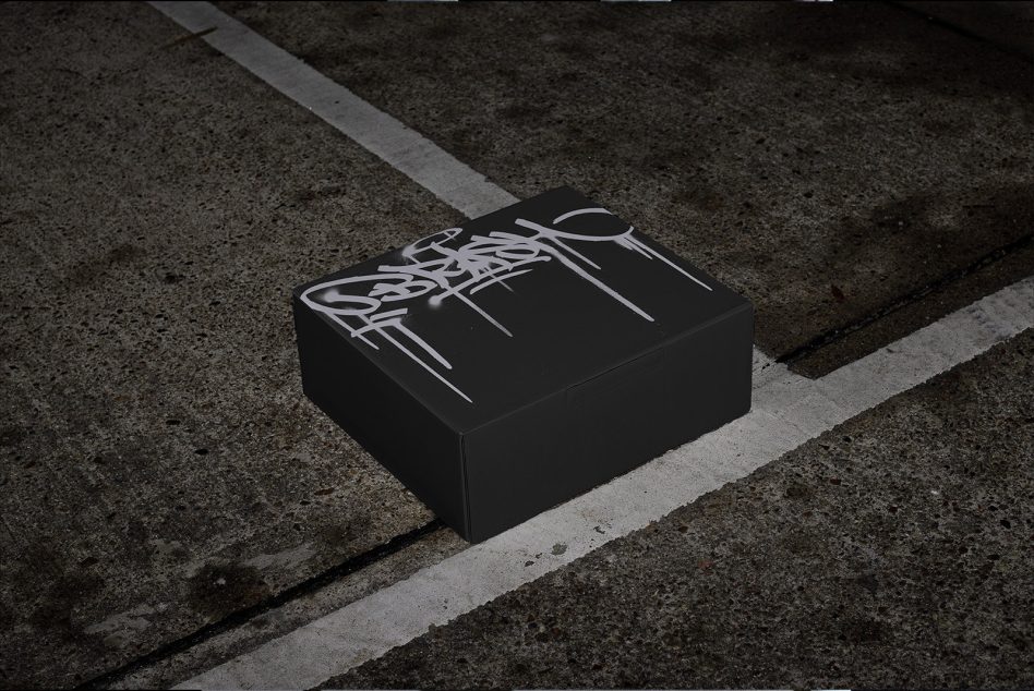 Black shipping box with graffiti tag on asphalt parking lot