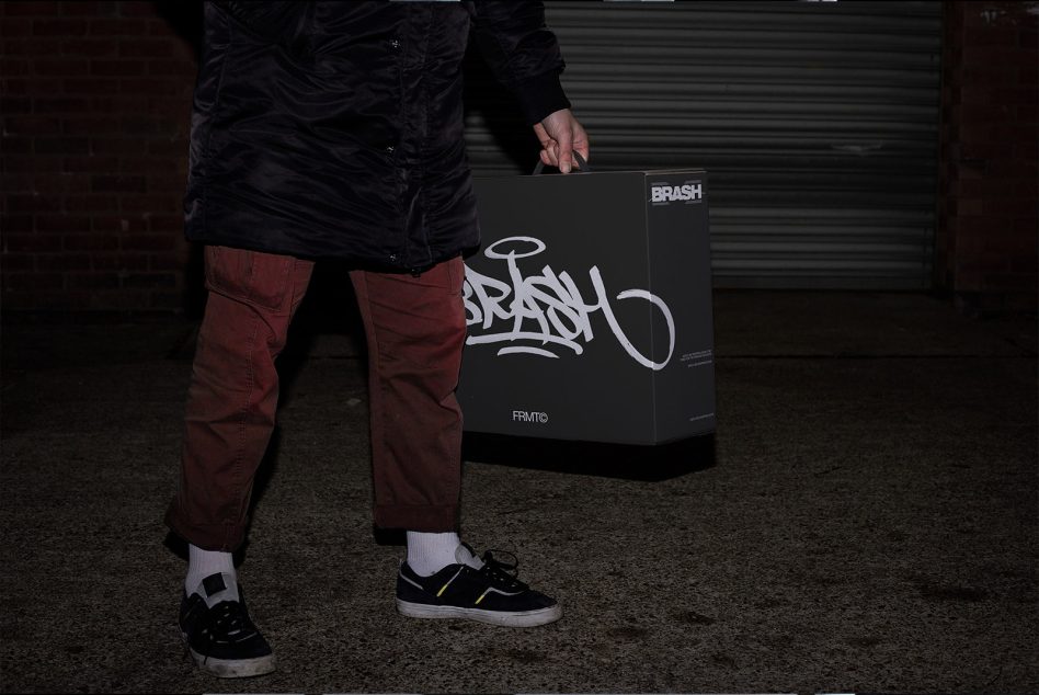 Dark charcoal rectangular box with white brash graffiti lettering being carried