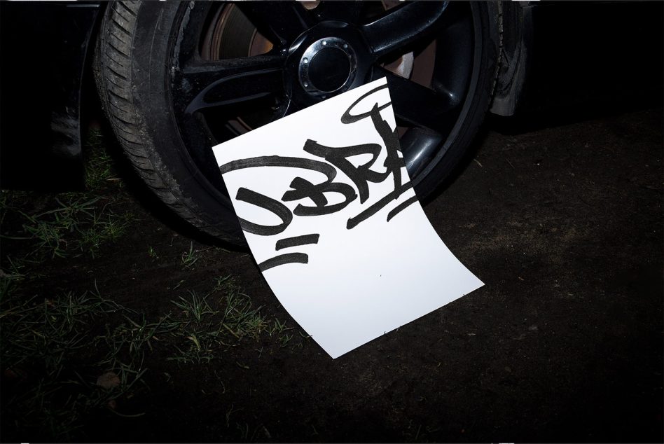 White paper propped against black car wheel with stylized script lettering