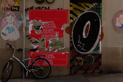 Red square poster with torn edges on wall by bicycle street art scene