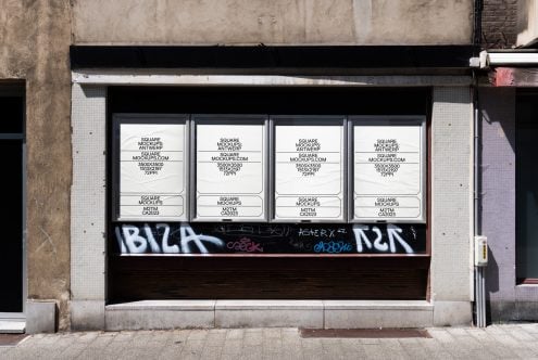 Four white square posters spanning storefront window, graffiti-tagged lower section