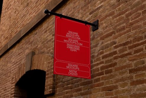 Bright red square sign mounted on brick wall with black metal bracket outdoors
