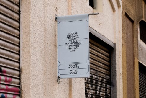 White square hanging sign on weathered brick wall between metal shutters