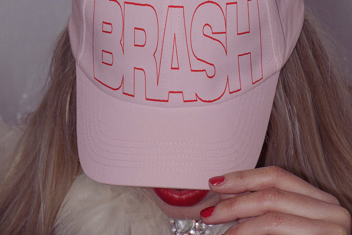 Person wearing pink baseball cap with bold red text mockup, vivid lipstick, fashion accessory for apparel design presentation.