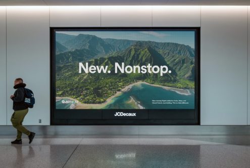 Large airport billboard displaying tropical island landscape with New. Nonstop. headline