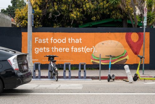 Urban street mural with fast food burger advertisement, bikes, e-scooters showcasing bold wall graphics design, ideal for mockup or template.