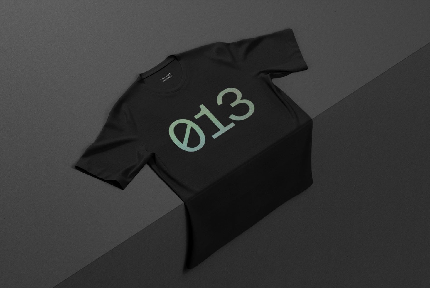 Black t-shirt mockup lying on a dark surface with a greenish number 013 design, ideal for apparel presentations and graphic design showcases.