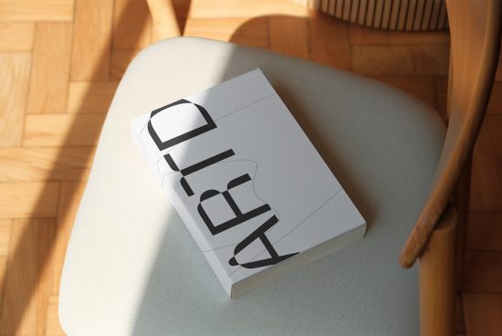 Mockup of a closed book with a custom typographic cover design on a chair in sunlight, showcasing realistic shadows and textures for presentations.