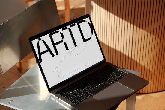 Laptop with graphic design on screen in a sunlit modern workspace, showcasing a bold font, ideal for mockup, fonts, and template design use.