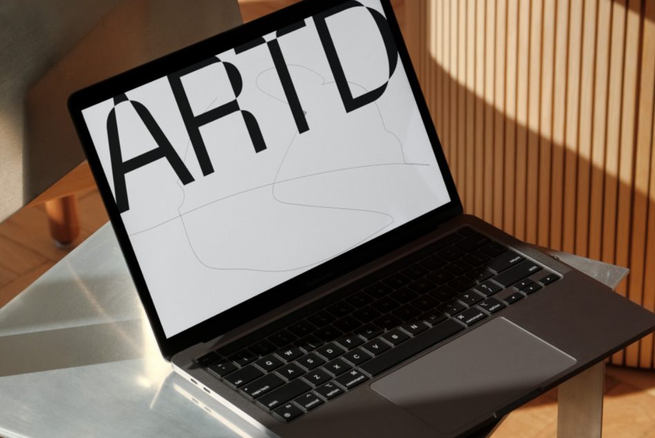 Laptop screen with bold black ARTD typography overlaid on minimalist line art
