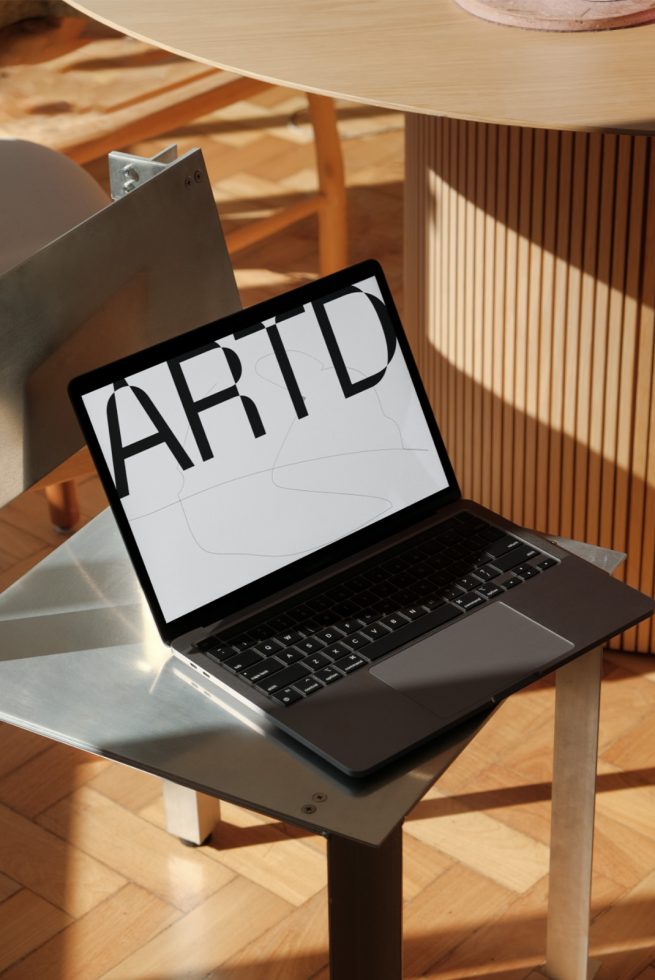 Laptop on metal stand displaying bold graphic font, ideal for mockup, modern typography, design asset, creative workspace setting.