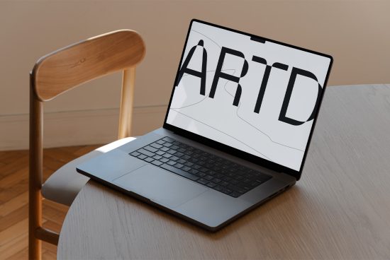 Laptop on wooden table displaying bold "ARTD" lettering, ideal for showcasing font design or graphic template in a natural light setting.