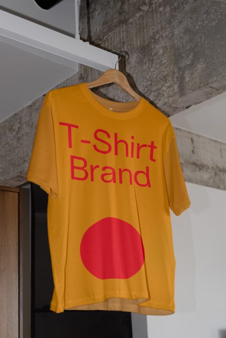 Gold colored tee hanging with text logo in red lettering