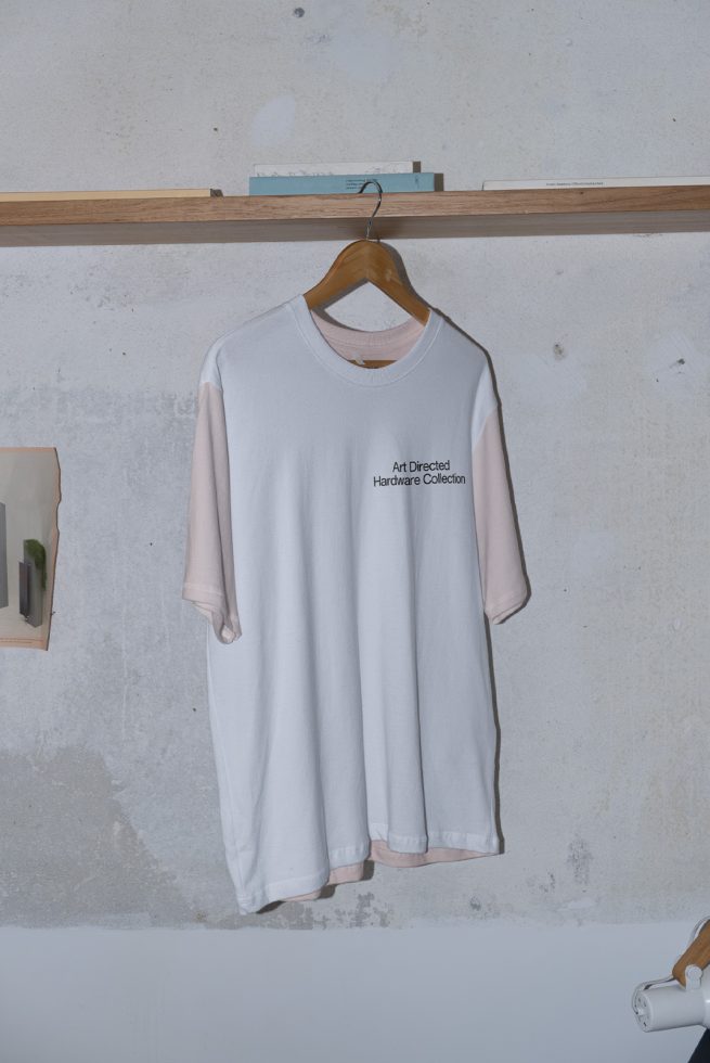 White t-shirt mockup hanging on wooden hanger against textured wall, ideal for presenting apparel designs and patterns to clients.