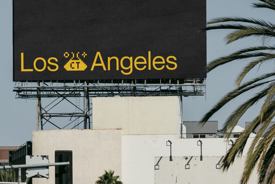 Black billboard with yellow Los Angeles lettering on metal structure beside palm