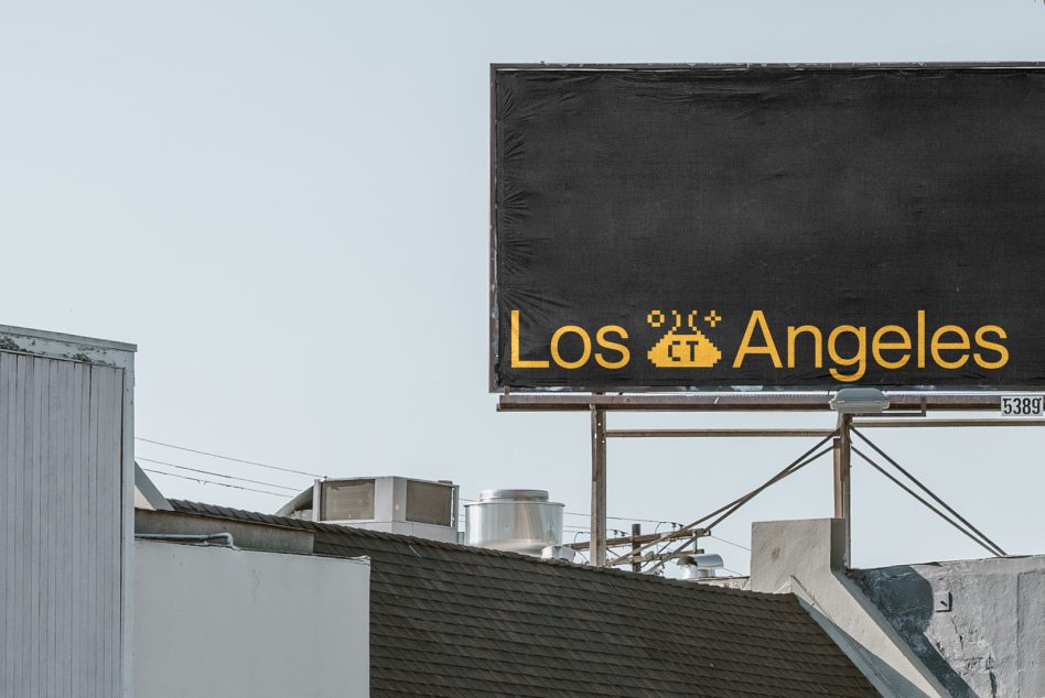 Dark billboard with yellow Los Angeles text on rooftop against industrial buildings