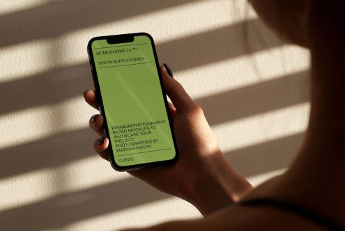 Person holding a smartphone with a green screen for app design mockups, shadow play on wall, ideal for UX/UI presentation.