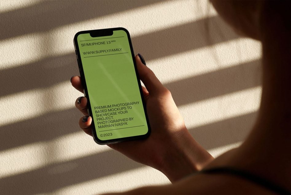 iPhone 13 Mini mockup with lime green screen in hand cast in natural light shadow