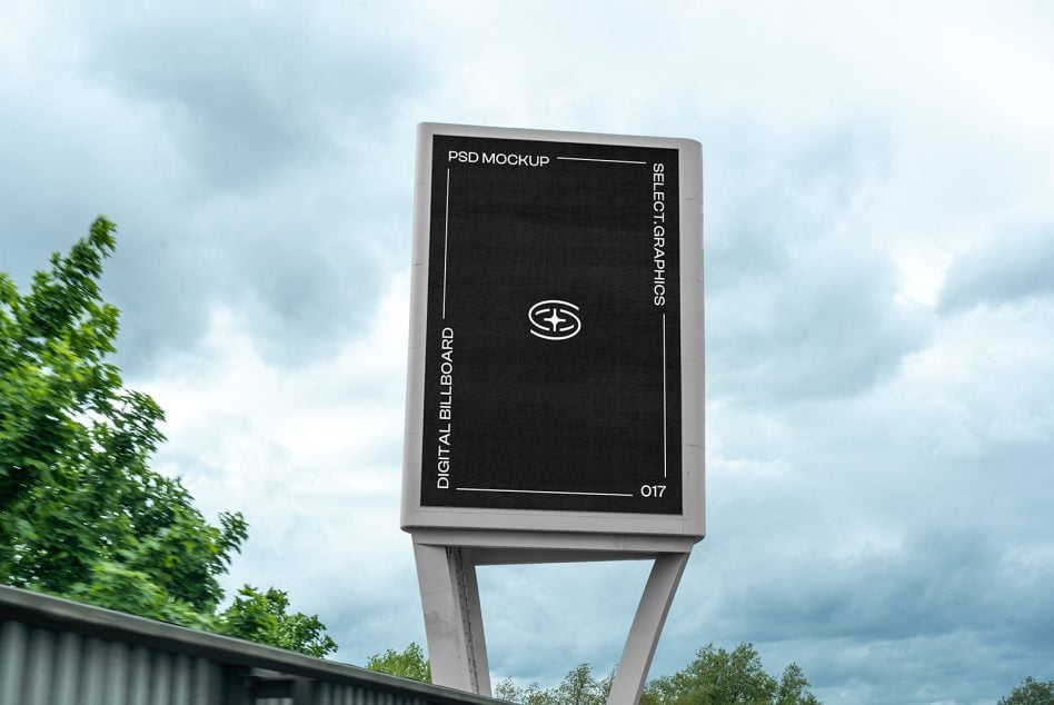 Dark digital billboard mounted on tall post overlooking highway with construction cranes behind