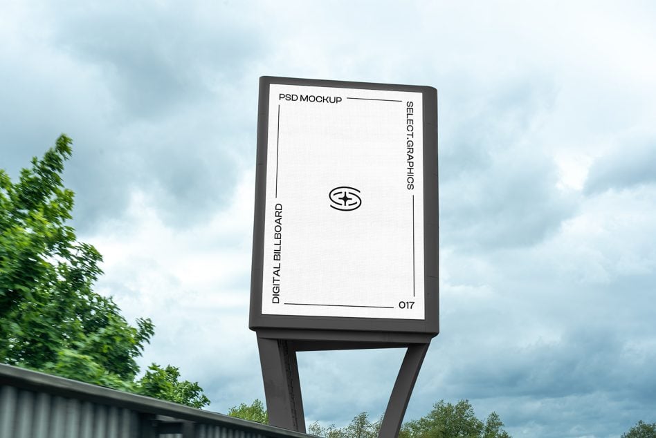 White digital billboard on tall post against cloudy sky with green trees on sides