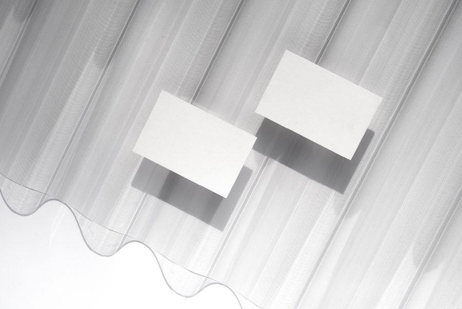 Two blank white business cards casting shadows on lined gray base