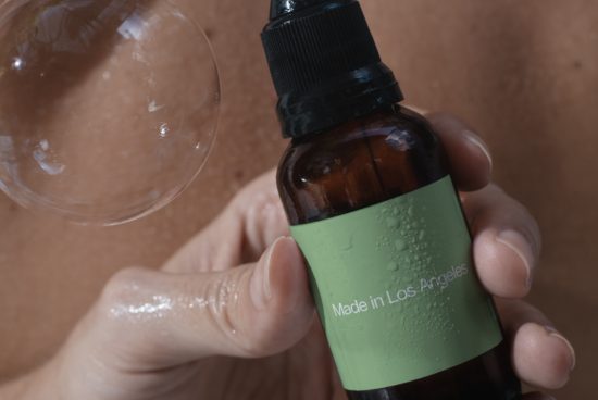 Close-up of a hand holding a skincare bottle with a green label, water droplets visible, perfect for mockup and product design.