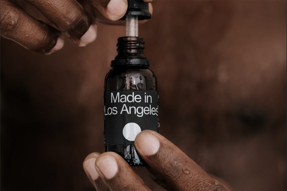 Close-up product mockup of a dropper bottle with "Made in Los Angeles" label held by hands, with a focus on natural branding and packaging.