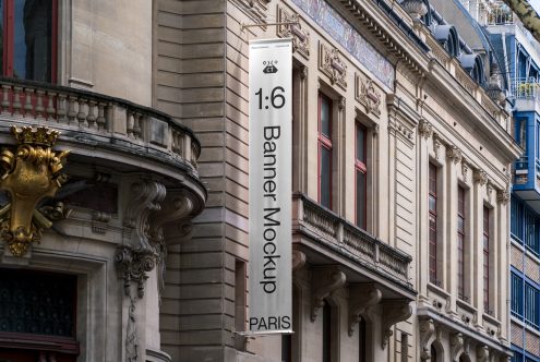White banner with black text hanging on stone building between ornamental architectural details