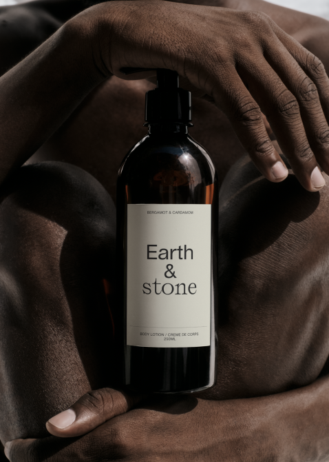 Hands holding dark amber glass bottle with Earth & stone body lotion label