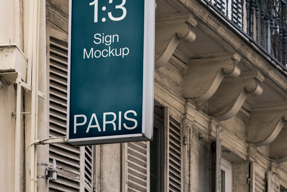 Teal hanging sign with white text on historic building facade in Paris