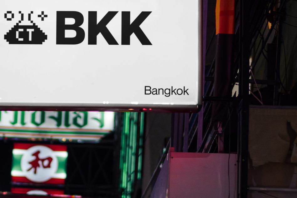 Large white horizontal sign with CT BKK pixel art logo above Bangkok street at dusk