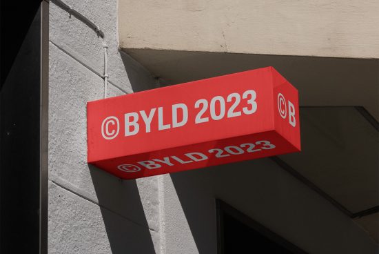 Red storefront signage mockup on building exterior corner with unique brand name BYLD 2023, clear skies, suitable for logo and branding designs.