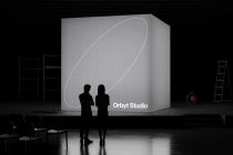 Two silhouettes facing large neutral tone display screen with curved line design