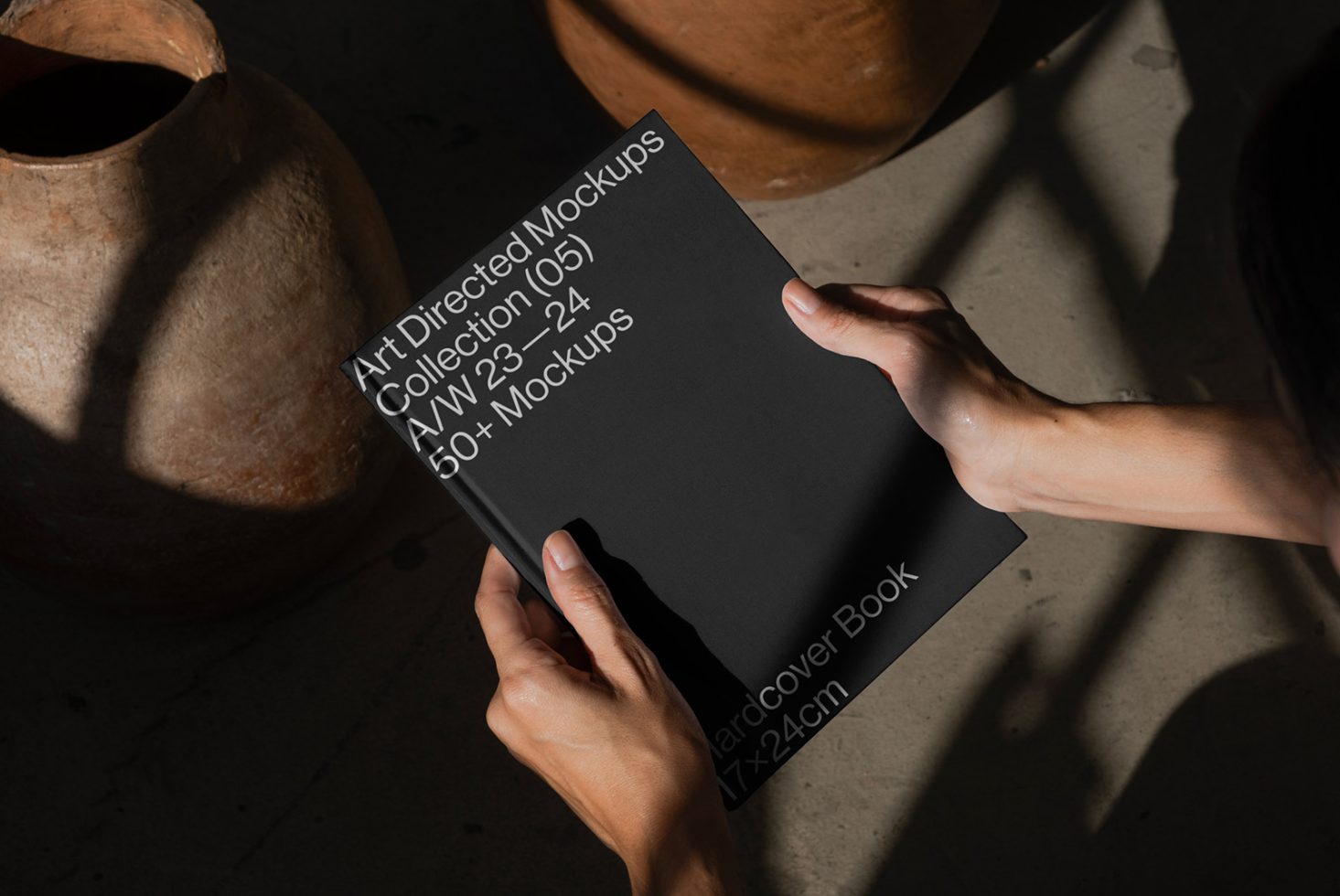 Hands presenting a hardcover book mockup against a textured background, shadow play, ideal for showcasing cover designs, includes editable layers for designers.