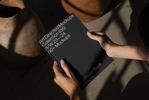 Hands presenting a hardcover book mockup against a textured background, shadow play, ideal for showcasing cover designs, includes editable layers for designers.