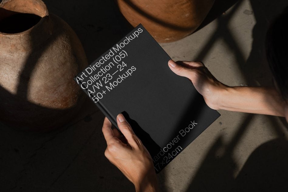 Hands holding dark book mockup with industrial background lighting