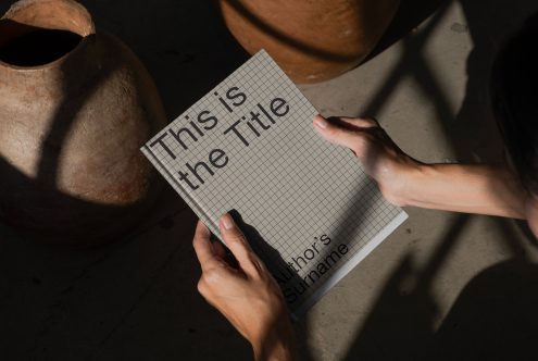 Hands holding a paper mockup with title text showcasing font and shadow play, ideal for designers presenting print templates.